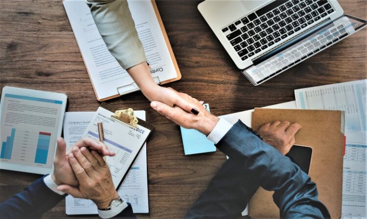 Homem e mulher dando as mãos para simbolizar um acordo fechado com uma terceira pessoa aplaudindo. 