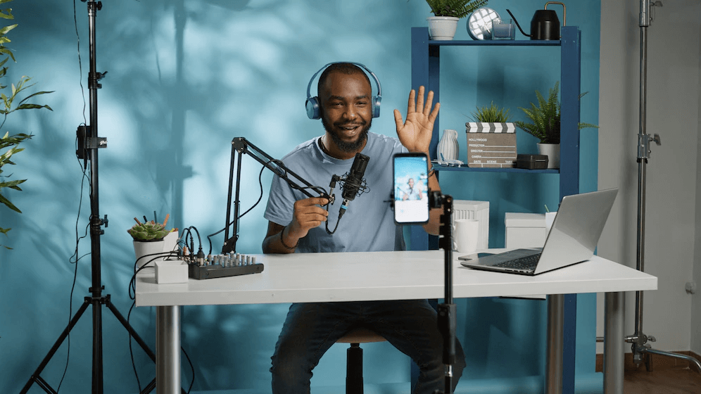 homem negro jovem se posiciona atrás de uma mesa branca e em frente ao celular para gravar mais um vídeo para o YouTube