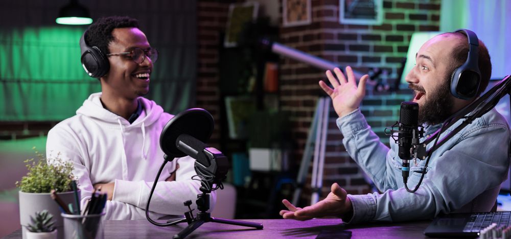 Dois rapazes conversando em uma mesa, com dois microfones.